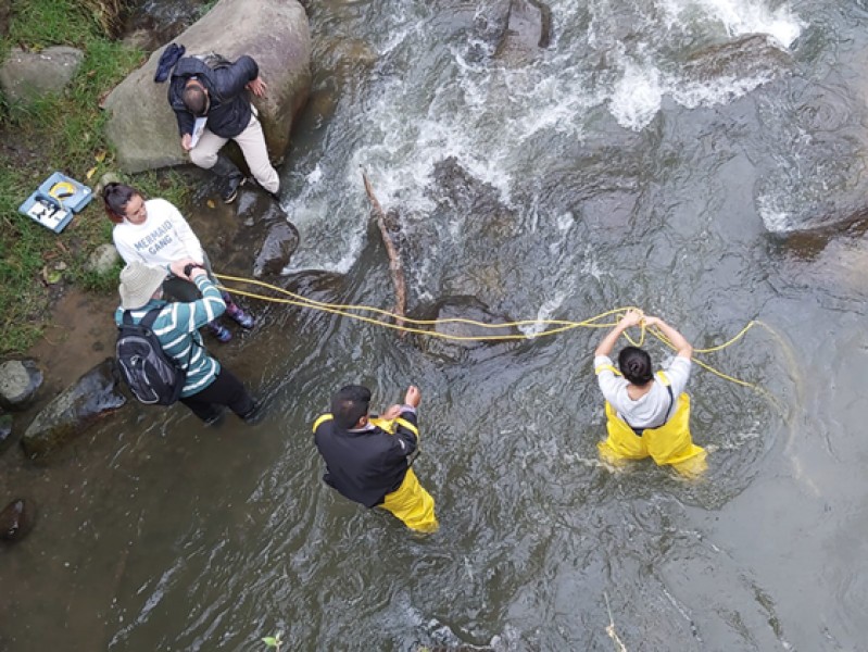 Hub and ASOCAMPO members are seen from above whilst wading in the Cauca River and using a multiparameter probe to take water quality measurements