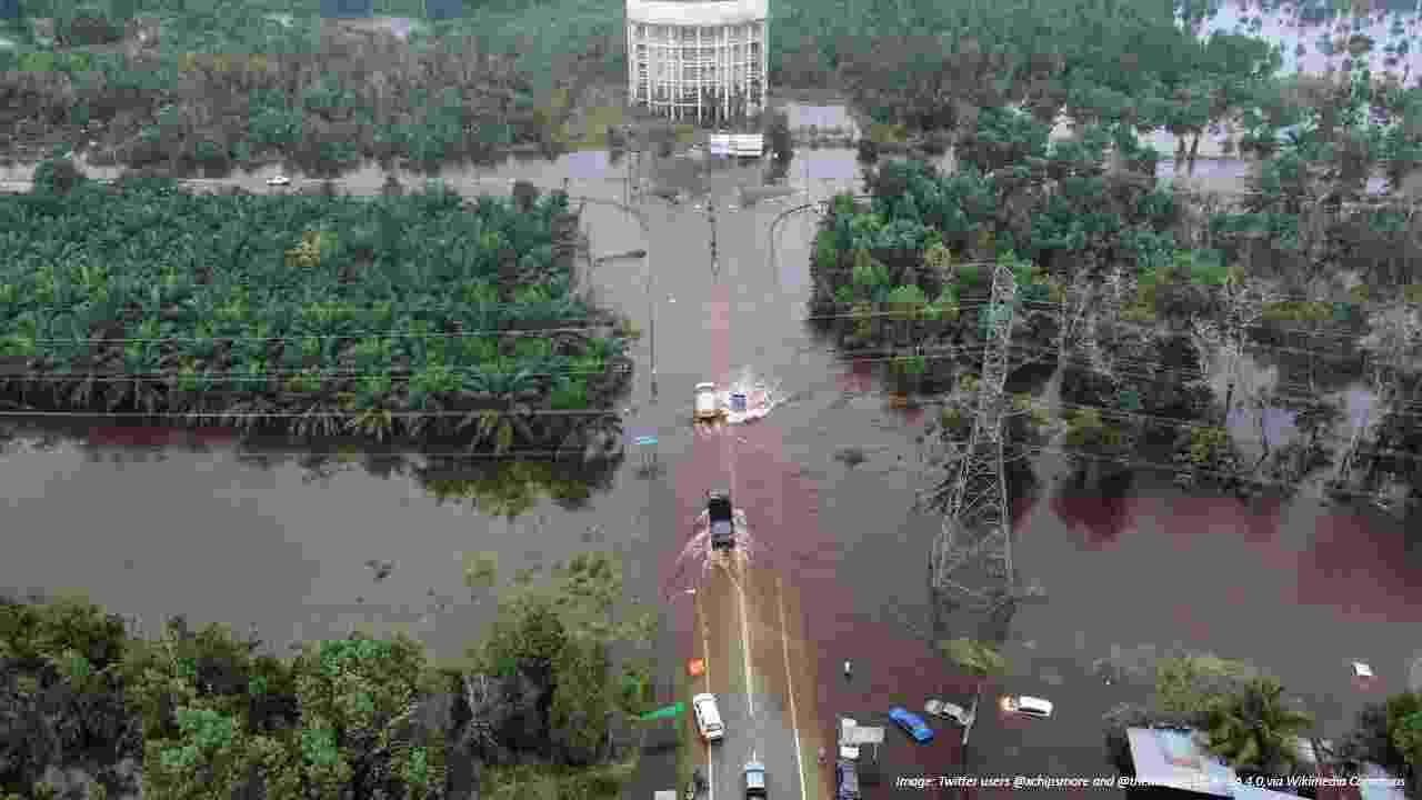 An aerial picture of dark red flood waters covering a road in Kuantan, Malaysia. Vehicles make waves as they attempt to cross. Submerged cars and vehicles can be seen elsewhere.