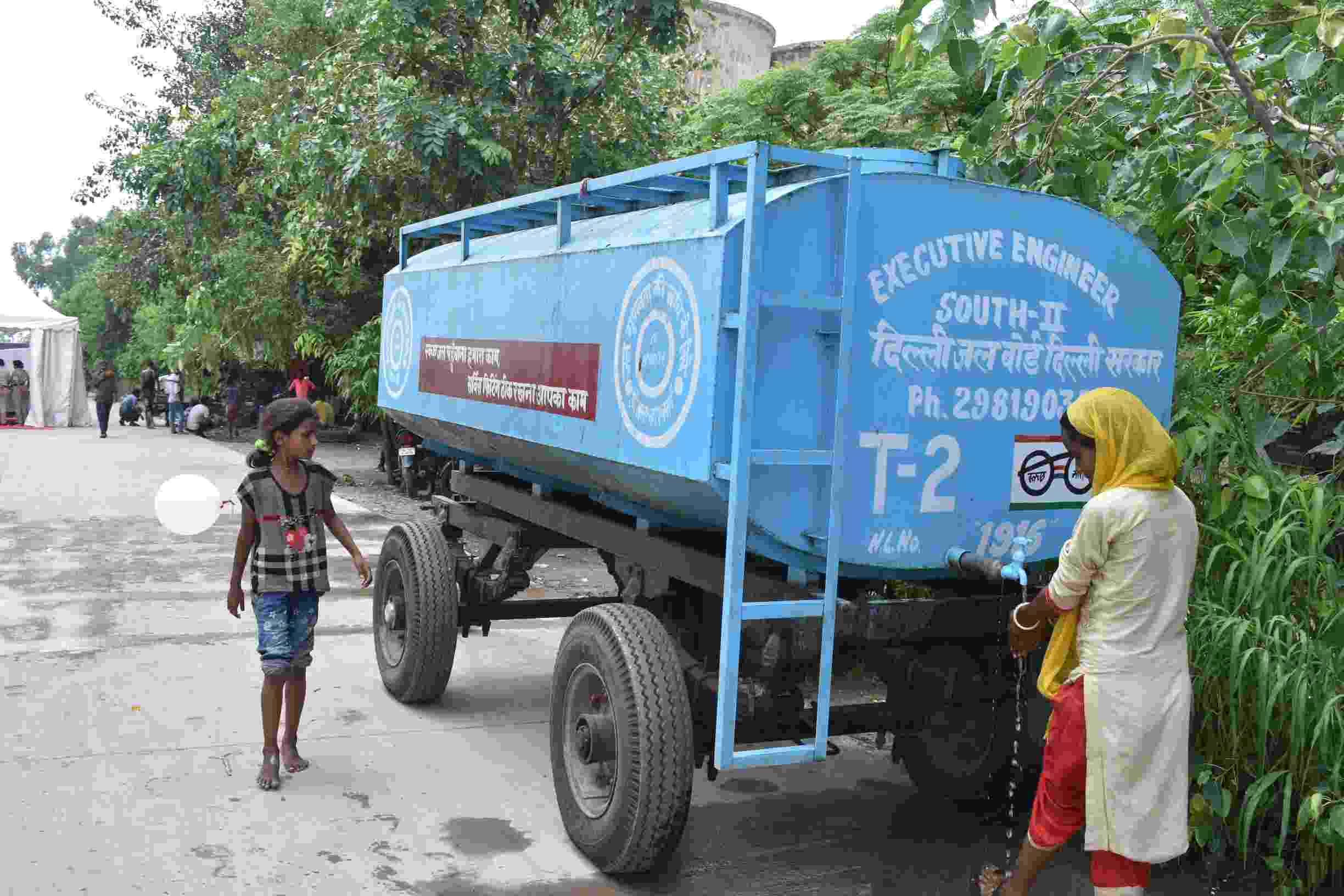Image shows people using a tank providing a supply of water to the Yamuna makeshift flood relief camps