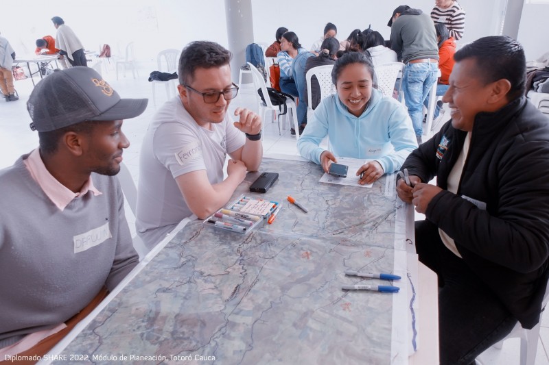 A group of people sit together around a table, annotating maps