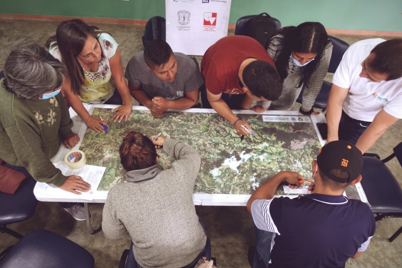 A top-down view of a group of 8 people stood around a table, annotating maps together