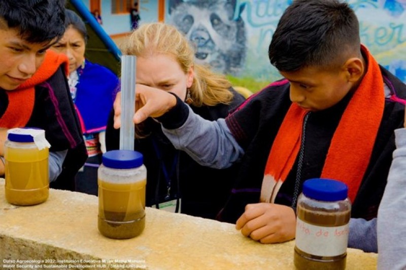 Participants of the agroecology course are stood together, carrying out soil analysis on three different soil samples