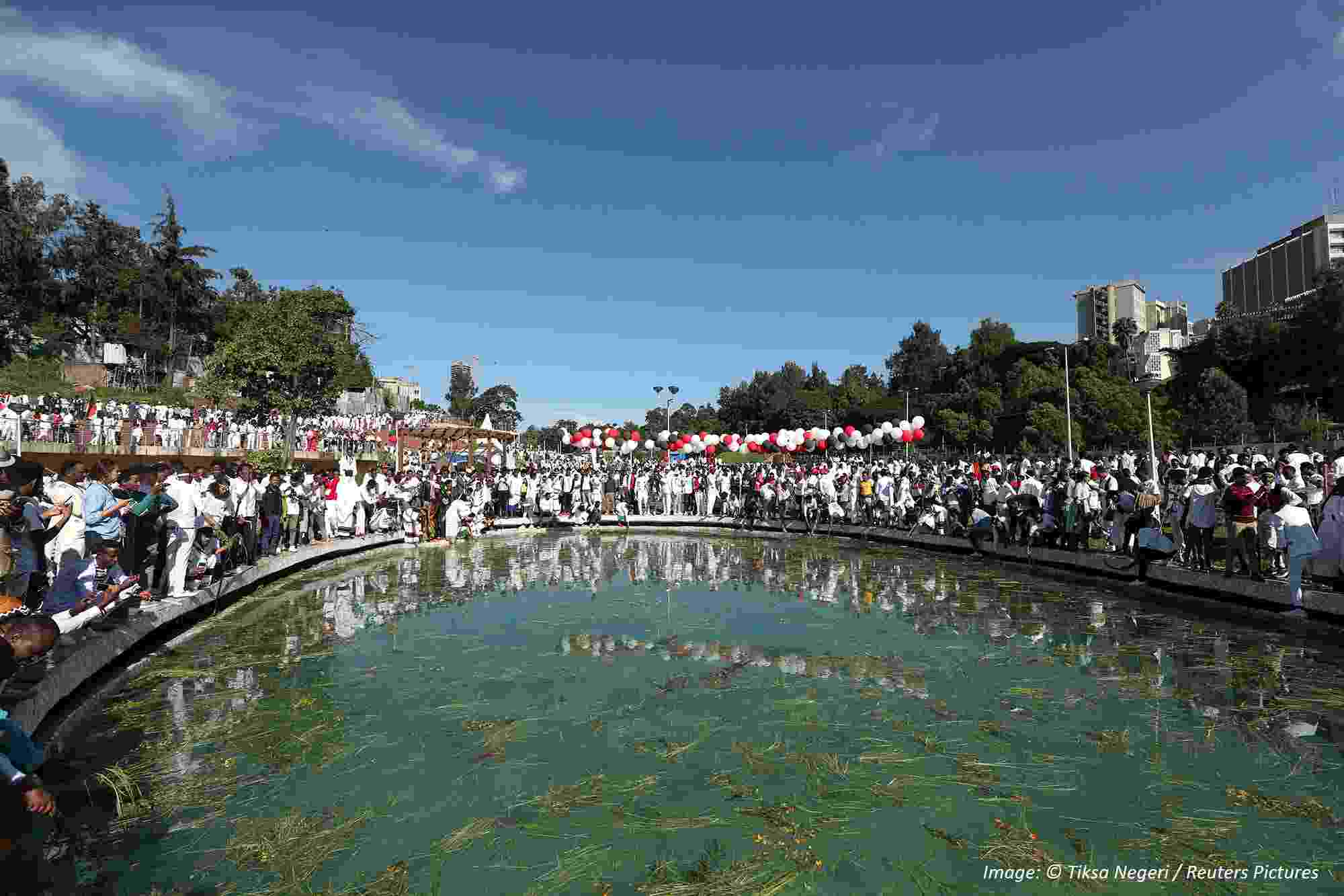 Image shows crowds of people gathered around a pond, celebrating Irreecha with colourful clothing and flowers