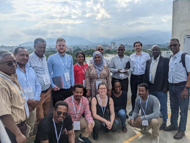 A mixed group of Hub members sat and stood together, smiling at the camera with the blue sky and mountains near Cali visible beyond