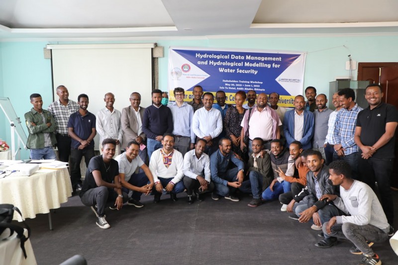 Workshop participants stand and crouch together in two rows in a conference room. The banner behind reads 'Hydrological Data Management and Hydrological Modelling for Water Security'