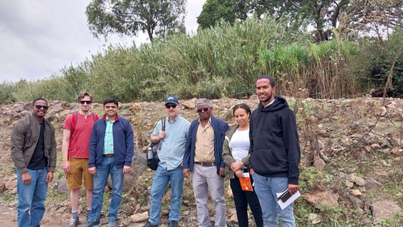 A group of Hub researchers stand together in front of a rocky built up mound, with green trees and shrubbery behind