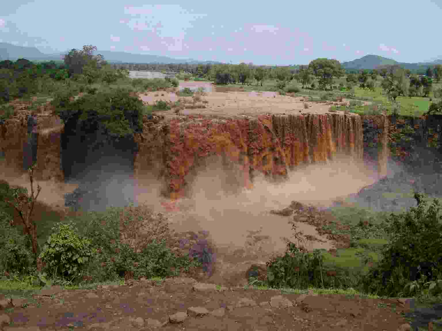 View from opposite bank of the Abbay River as it cascades down the Nile Fall during the monsoon season; the water is coloured red from soil and sediment