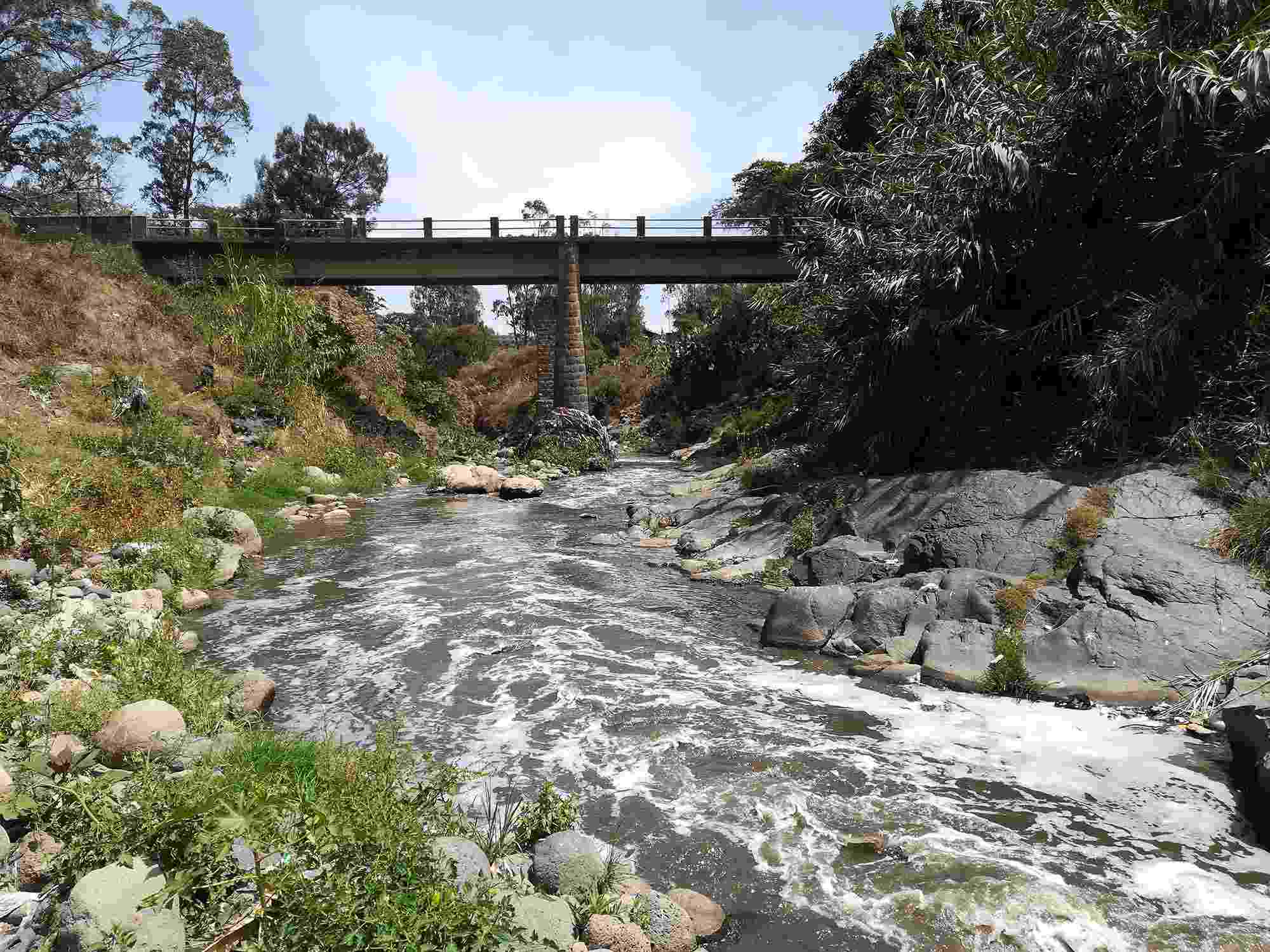 The Akaki River flows downstream under a bridge and past rocks and trees, picking up more pollution as it passes through Addis Ababa, the capital city of Ethiopia