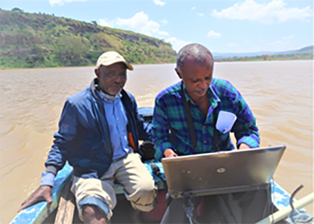 Hub colleagues sit with a laptop and equipment in a small fishing boat on Lake Harebata to conduct a hydrographic survey of the lake, Ethiopia