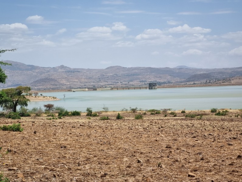 Wide view of a reservoir surrounded by dry shrub and grassland, with a mountain range behind