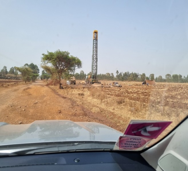 View from the dashboard of a car, looking out on water drilling equipment in a dried crop field