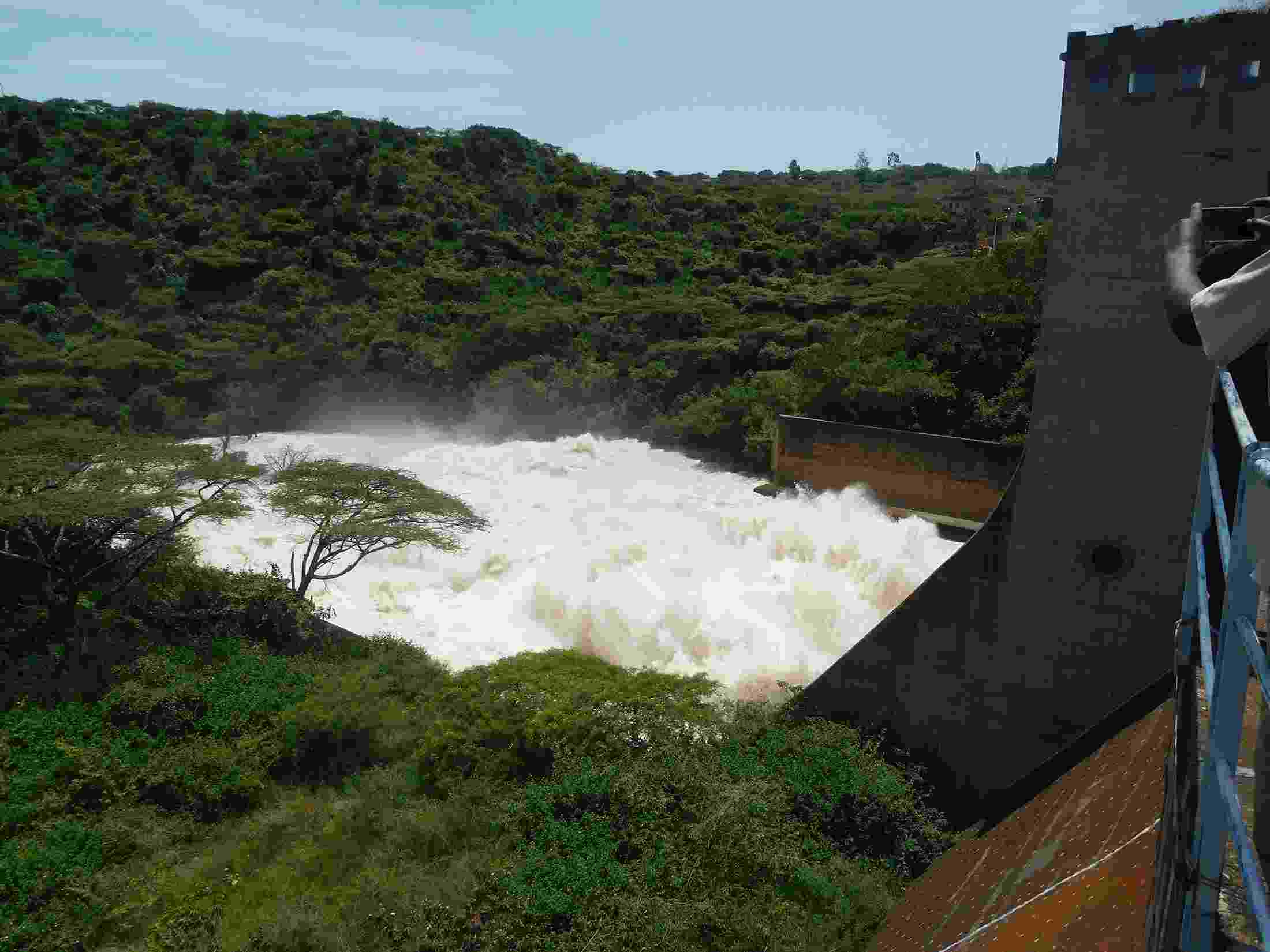 Over-the-side view from the Koka Dam on the Awash River, with water surging out from an opening in the dam, surrounded by lush greenery