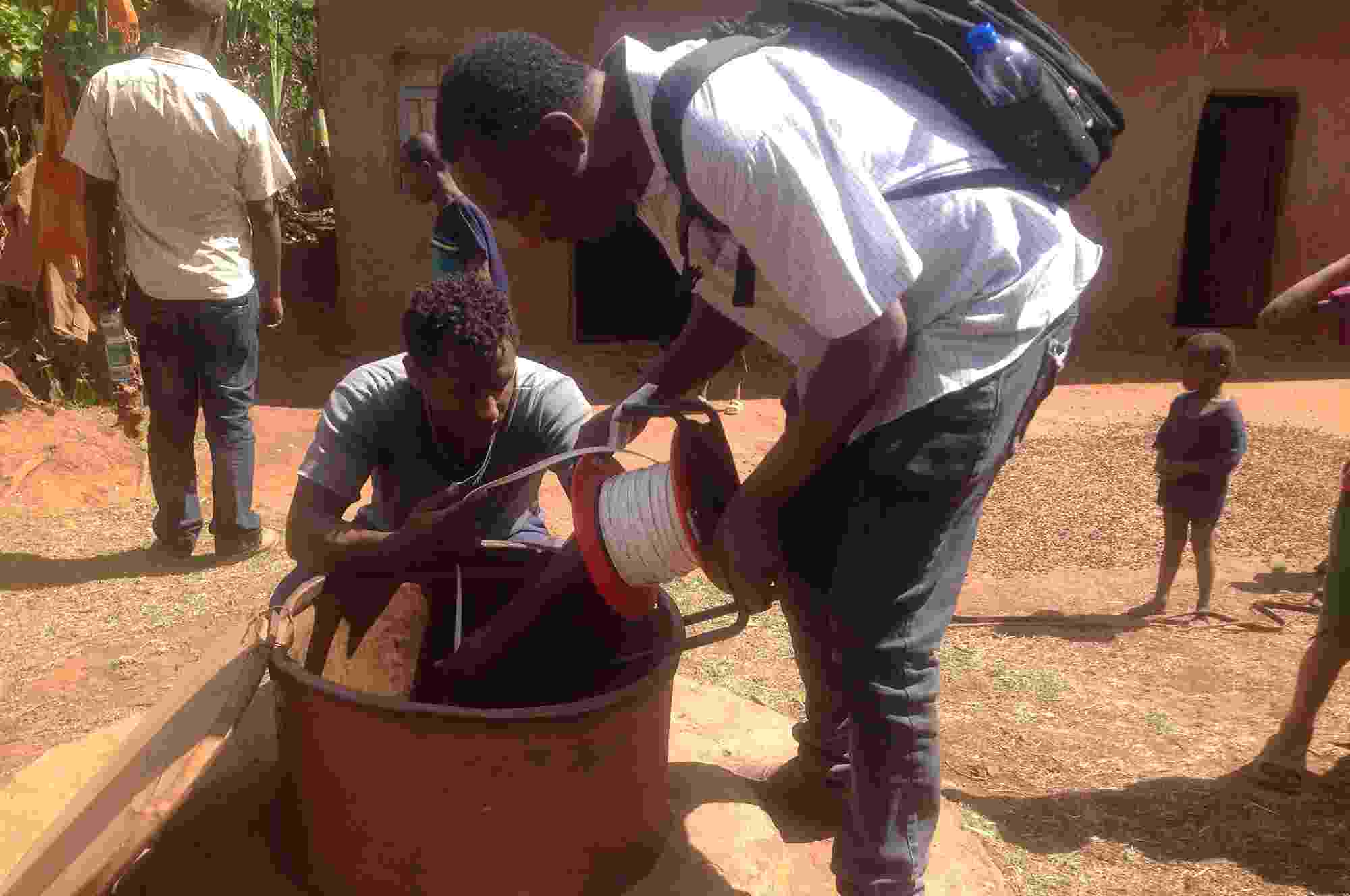 Two citizen scientists use simple equipment (a plastic bucket tied to a long length of string) to measuring shallow groundwater levels via a borehole, Ethiopia