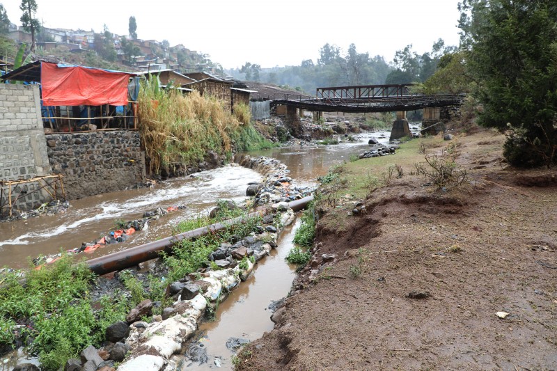 The river is visibly full of pollution and solid waste as it flows under a bridge and past residential buildings