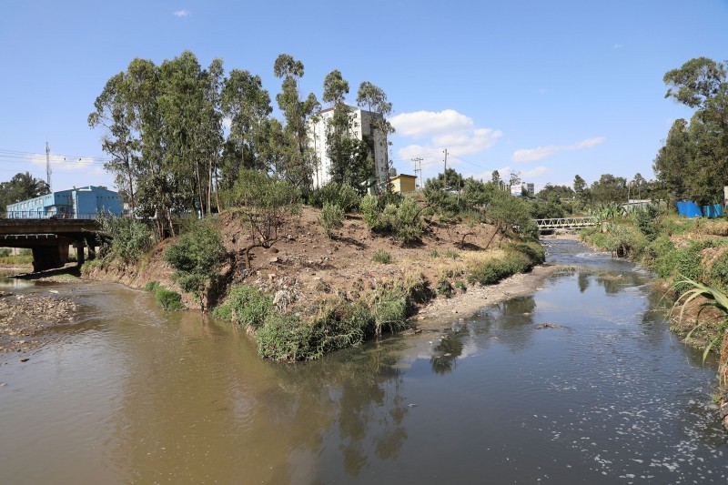 The Little Akaki River flows either side of a bank covered in vegetation, and residential and factory buildings