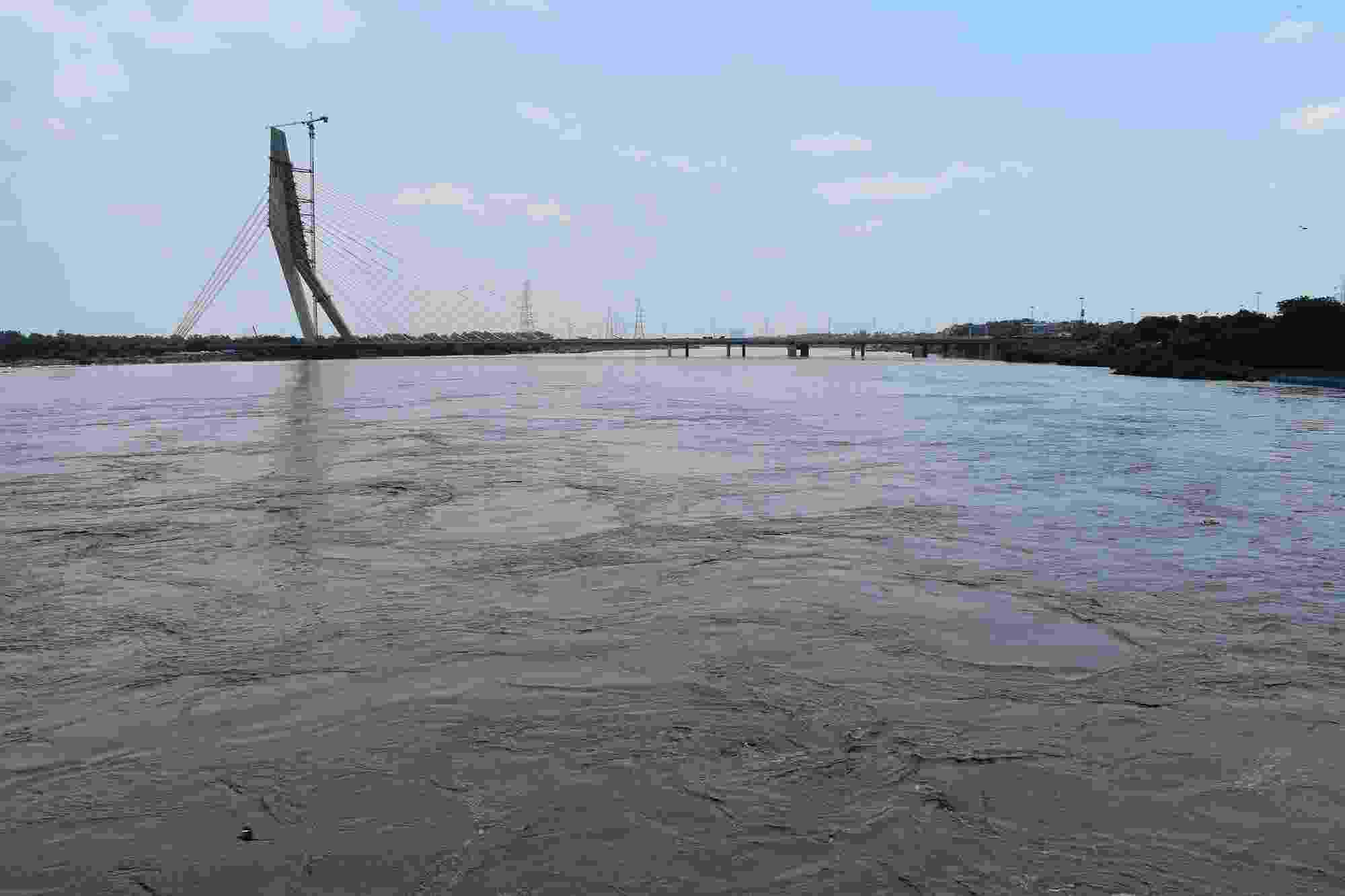 The flooded expanse of the Yamuna River fills the photo, with the Signature Bridge crossing the river and parts of Delhi's skyline visible in the distance 