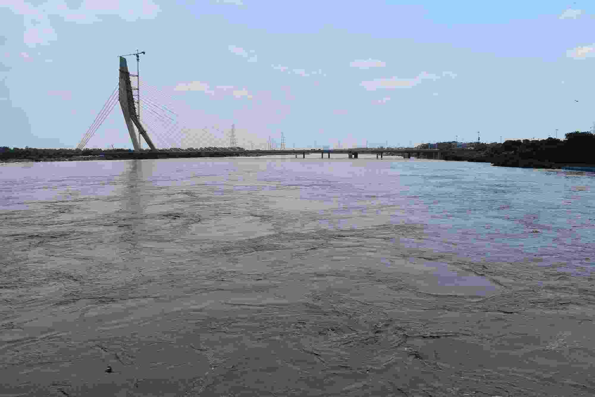 The flooded expanse of the Yamuna River fills the photo, with the Signature Bridge crossing the river and parts of Delhi's skyline visible in the distance