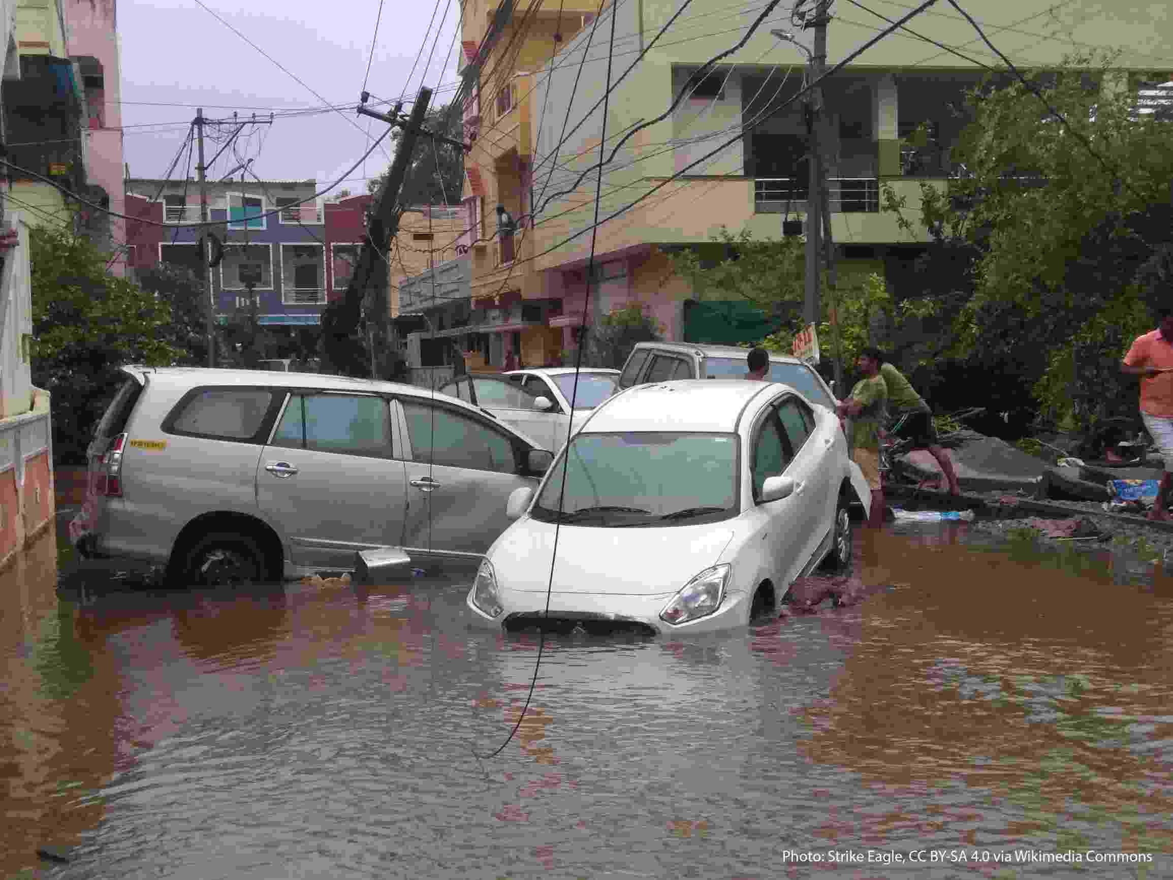 Several cars are partially submerged in flood waters in Hyderabad. The strength of the water has swept the cars down the street between houses, and damaged powerlines are visible behind