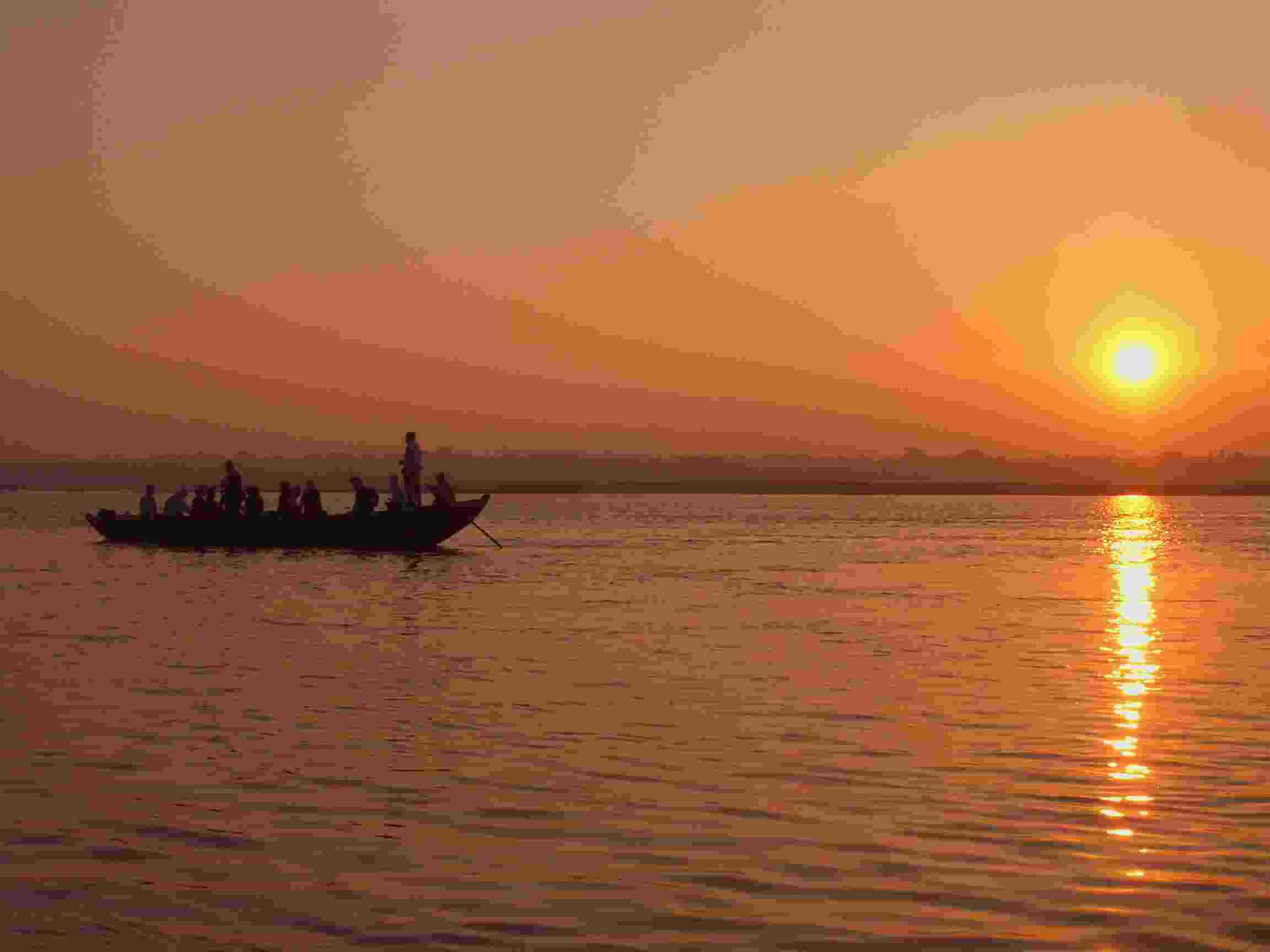 The silhouette of a boat filled with several people against the orange dawn sky and silver-coloured water