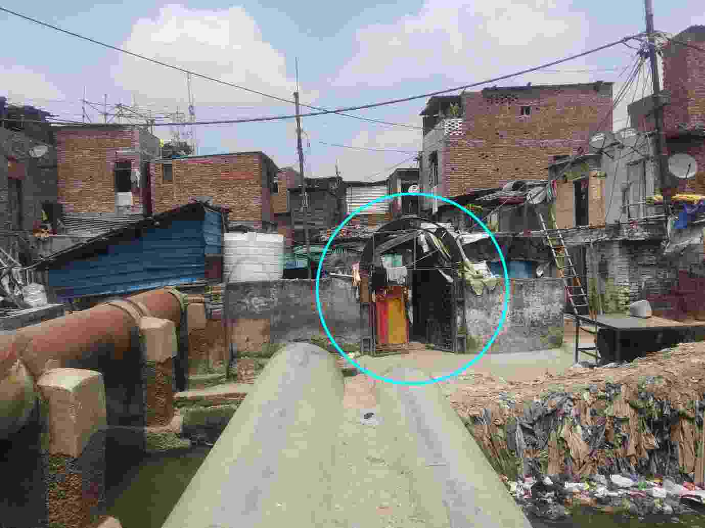 Buildings made from mud and sheets of iron, and bricks, that form part of the Indira Camp Part-II, with a small entrance to the community toilet