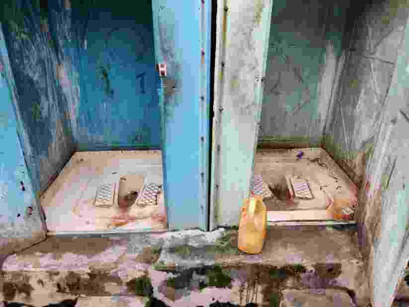 Two poorly maintained and poorly cleaned portable toilets situated next to each other with limited privacy and no water connection