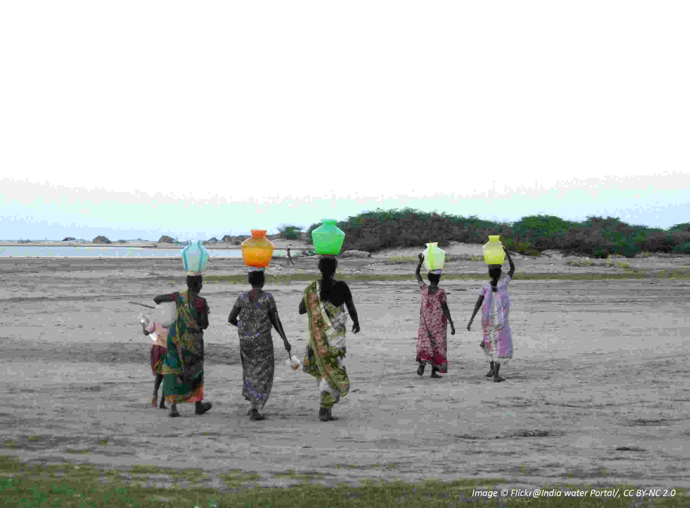 Five women walk away across dry, open land, each carrying water in a colourful vessel on their head