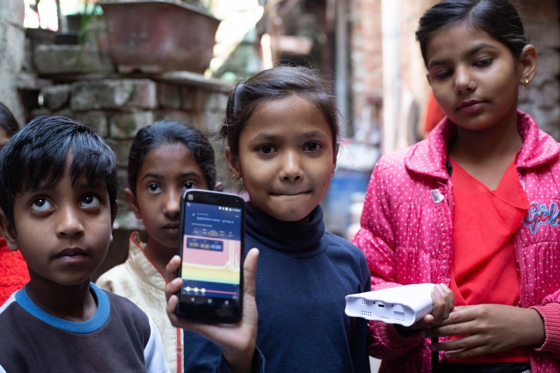 A group of school children hold up a piece of air quality testing equipment to the camera