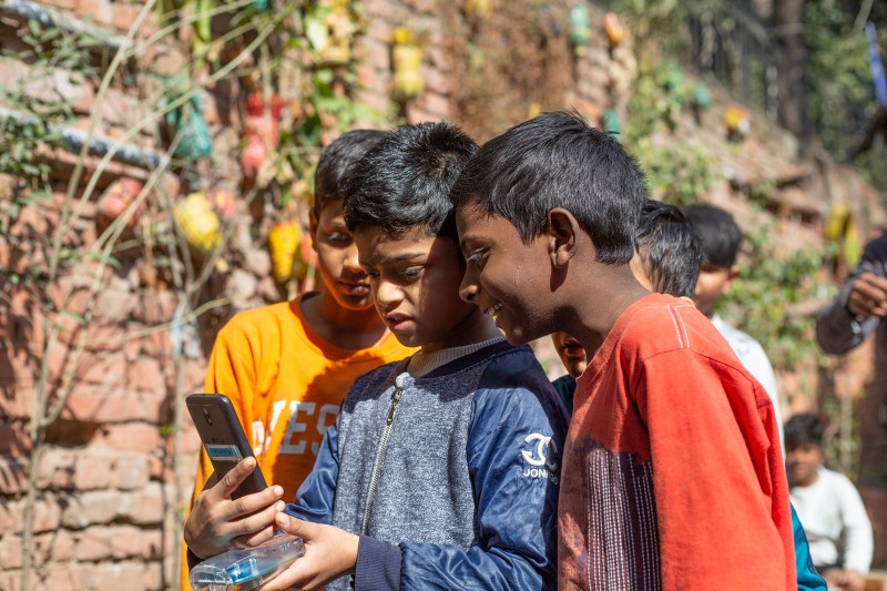 Three young school children lean together to look at air quality testing equipment