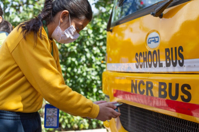 A school pupil holds up an air quality sensor to a yellow school bus