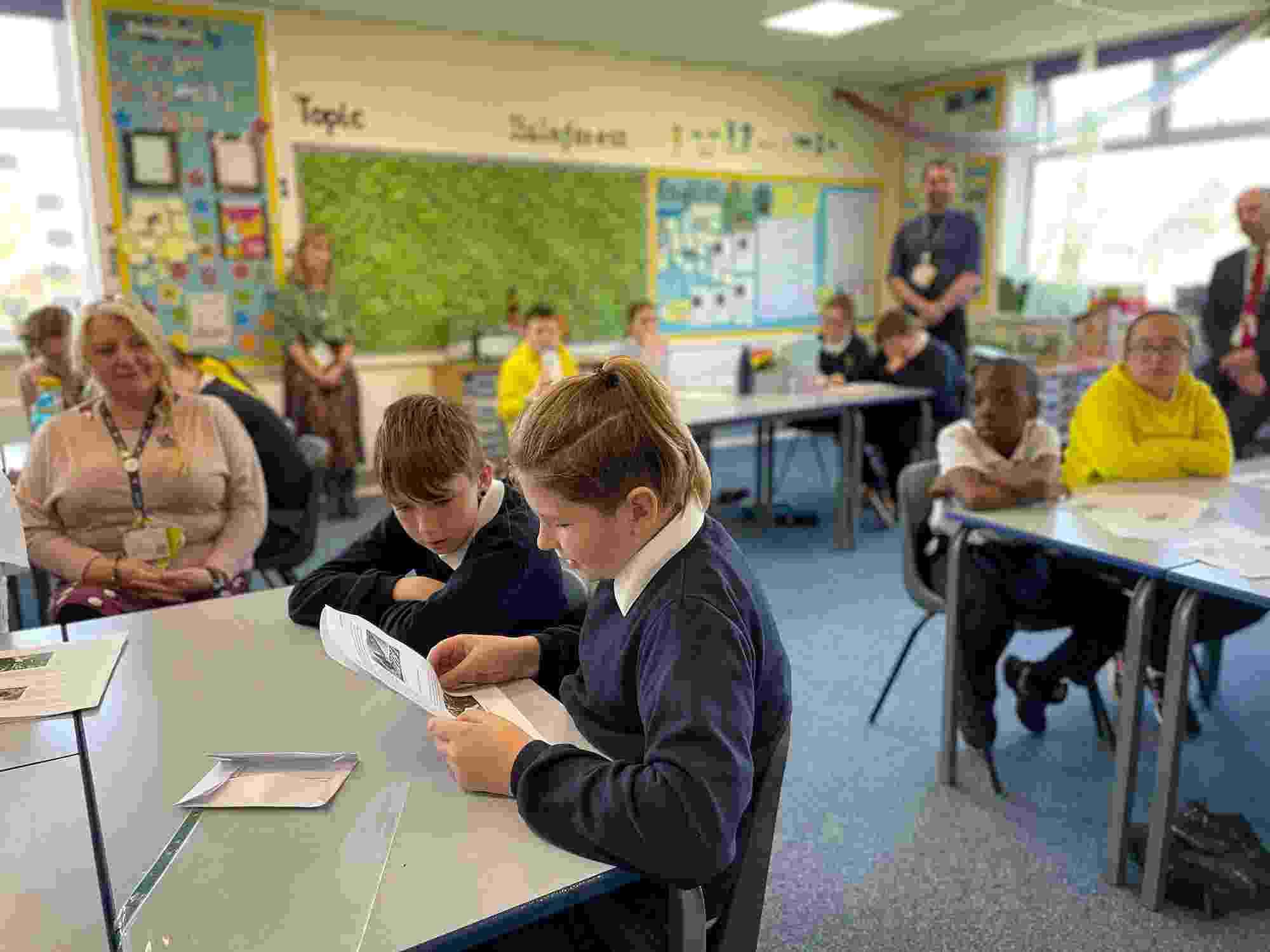 Two schoolchildren from Percy Main Primary School read out questions for the local mayor from their desks, while fellow students and teachers look on from the background