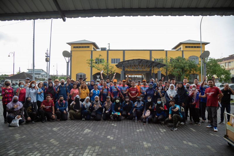 Over 40 World Environment Day event participants smile and stand together for a group photo, with some kneeling in the front row, and others waving their arms in the air.