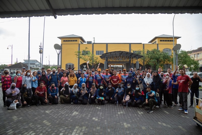 Over 40 World Environment Day event participants smile and stand together for a group photo, with some kneeling in the front row, and others waving their arms in the air. 