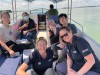Six Hub members smile and lean in for a photo on the back of a boat, with an open expanse of water on either side.   thumbnail