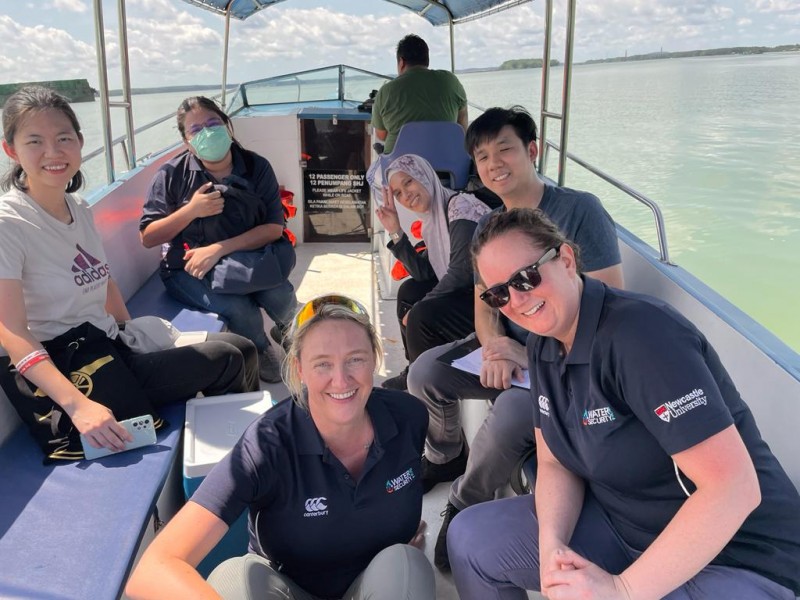 Six Hub members smile and lean in for a photo on the back of a boat, with an open expanse of water on either side.  