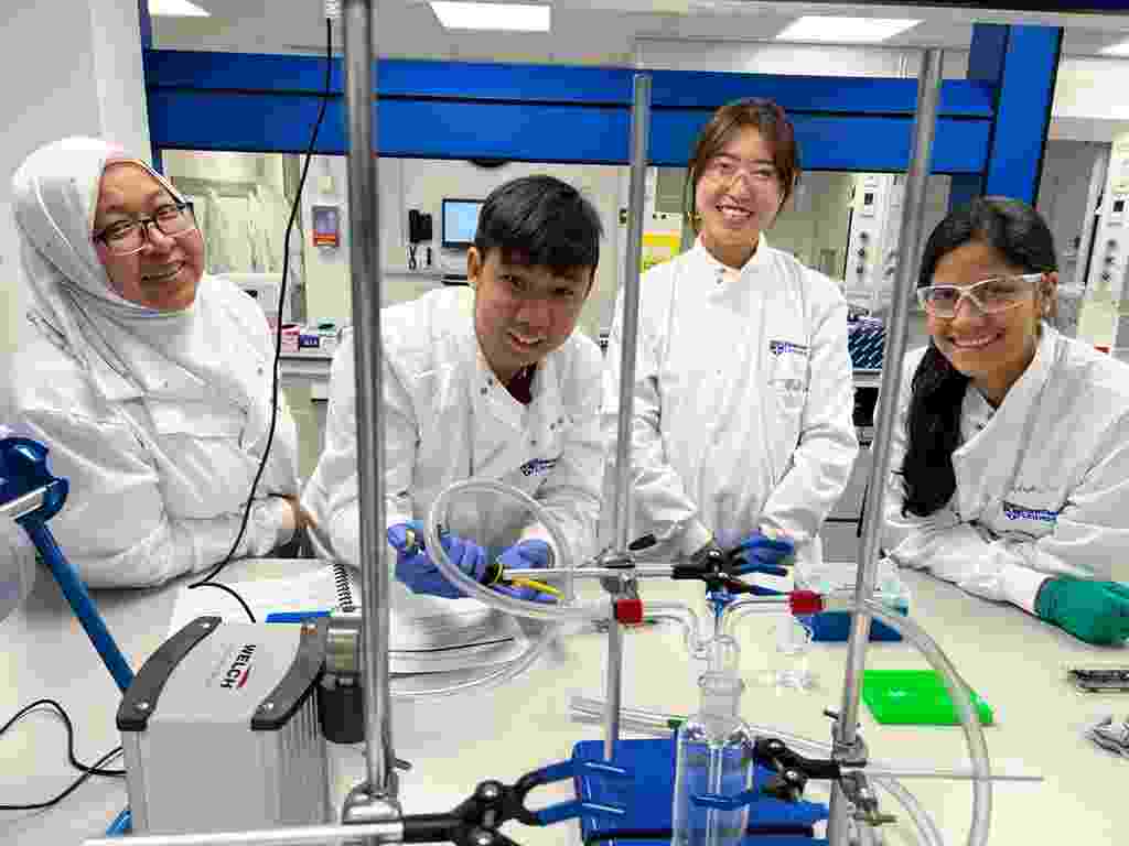 Four members of the NUMed team, wearing protective lab clothing, work a laboratory bench using water quality analysis tools