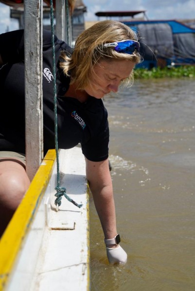 Michaela, from the NUMed team, leans out and collects a water sample over the edge of a boat