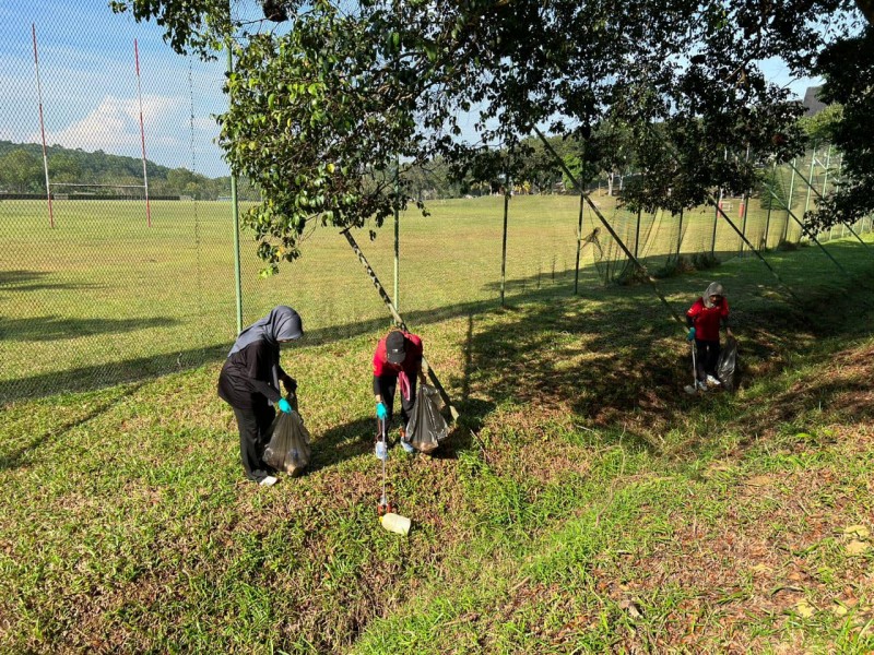 Three women use litter pickers to collect waste from a lush green sports field