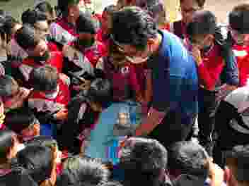 A group of children gather round while a Hub researcher gives a demonstration using props