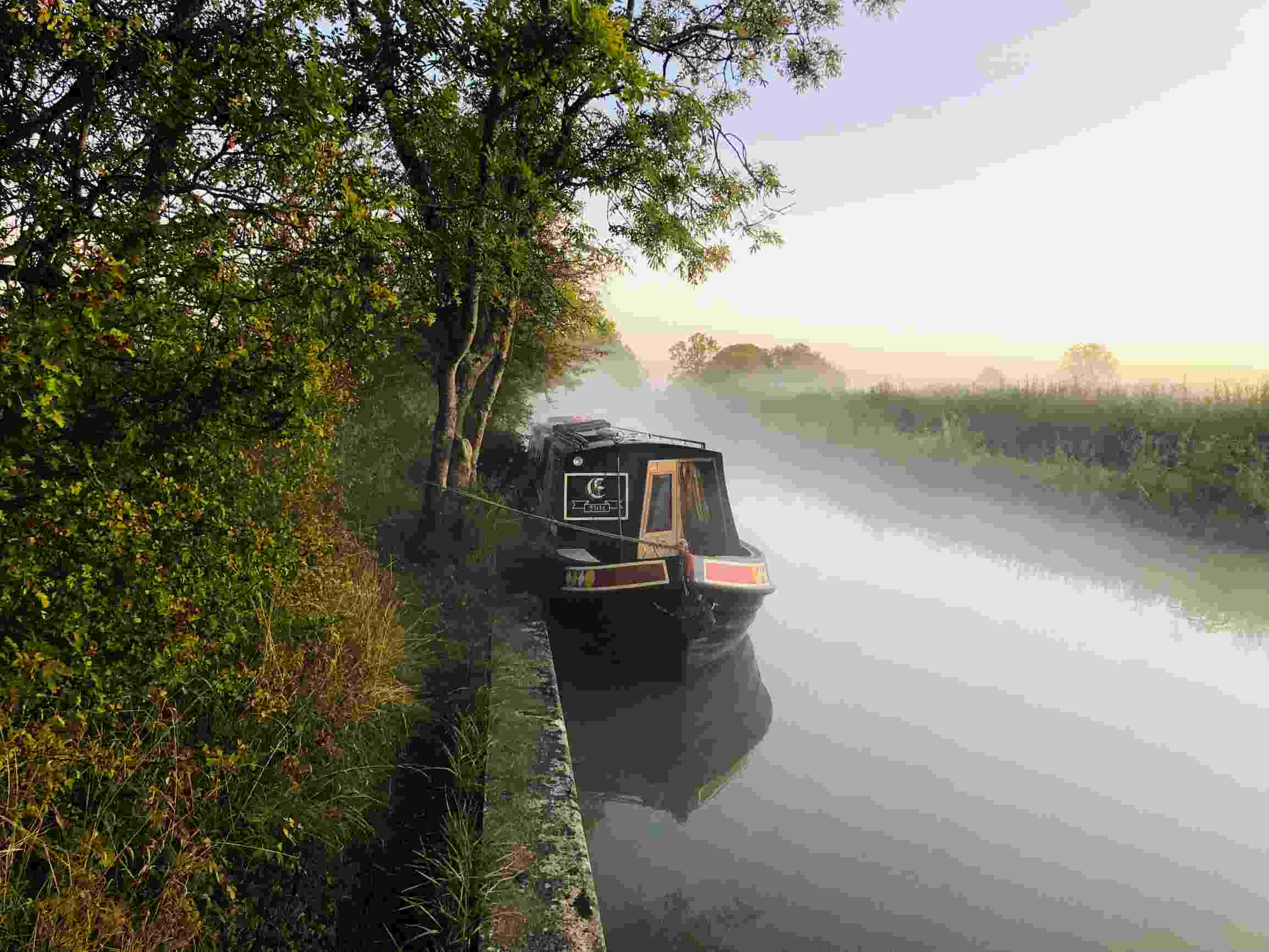 A moored canal boat against a mist-covered water surface
