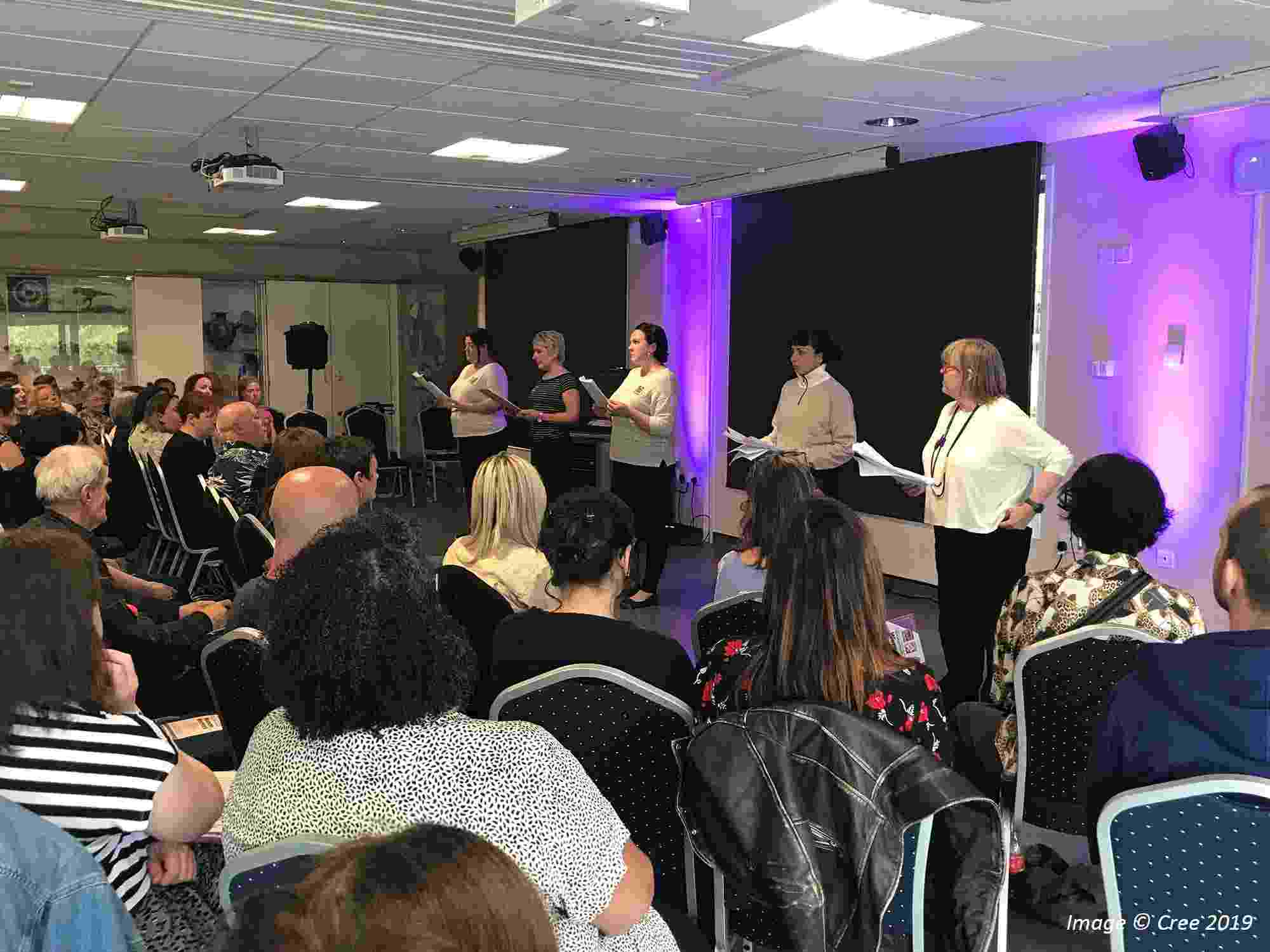 A view across the audience of five women on stage performing a reading of 'Women Warriors' at the Workie Ticket Theatre CIC, 2019